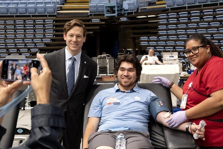 A blood donor poses for a photo with a nurse  and Chancellor Roberts on either side of them.