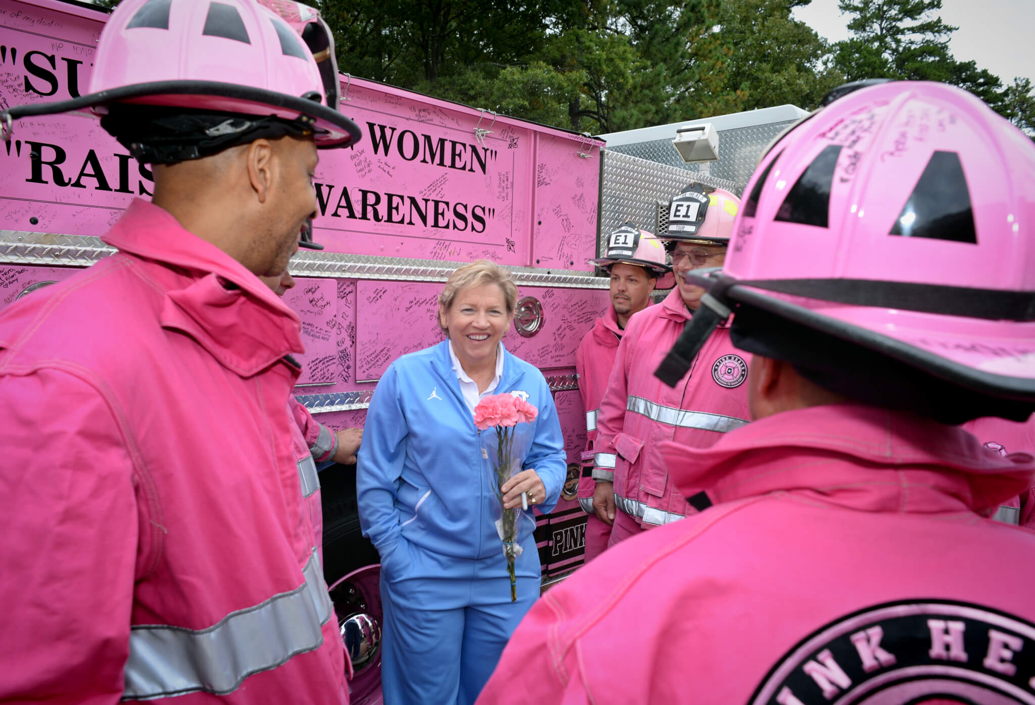 Sylvia Hatchell holds pink flowers and talks with firefighters dressed in pink uniforms