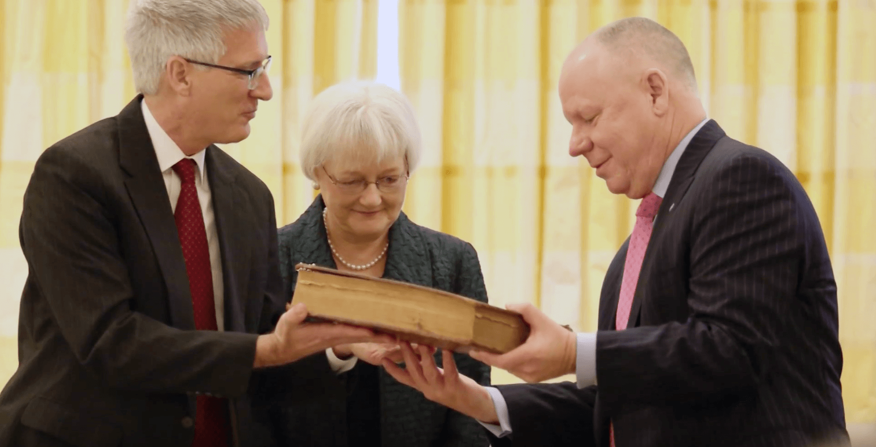 Three people gather to admire an old book.