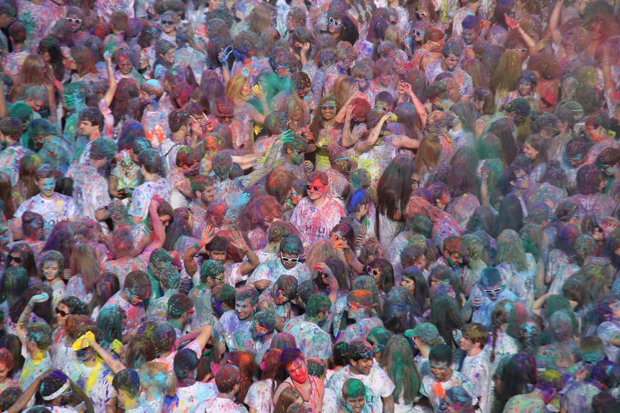 Powders of blue, pink, yellow, green and orange fall on a crowd of students wearing white shirts