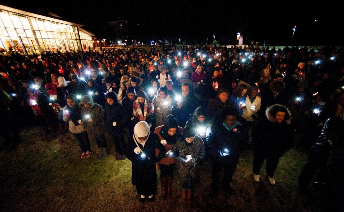 Group of people bow their heads with lights in their hands.