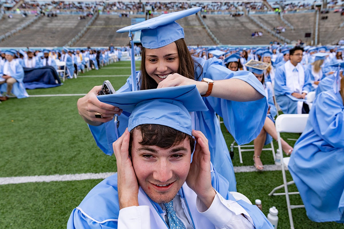 A graduate fixes another's cap.
