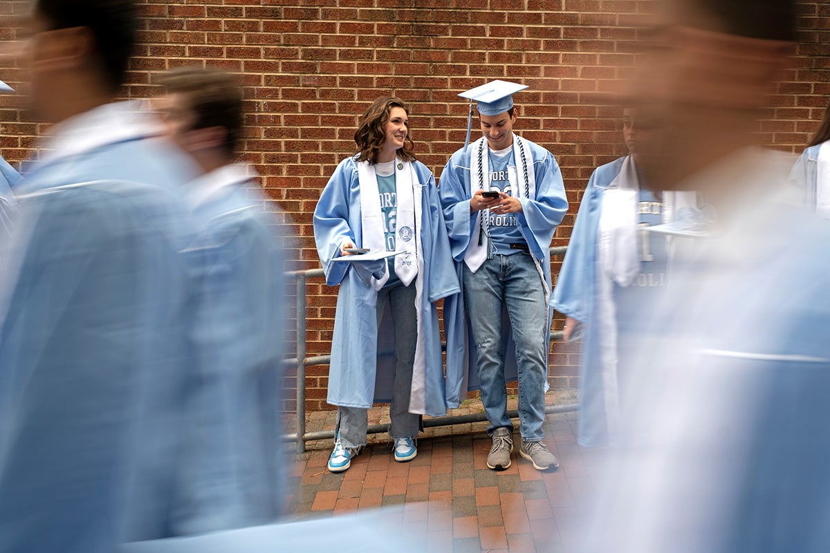 Two graduates standing as others walk past.