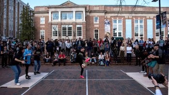 Indi Cowie juggles a soccer ball while the Dorrance Dance troupe dances on both sides of her and a crowd watches on