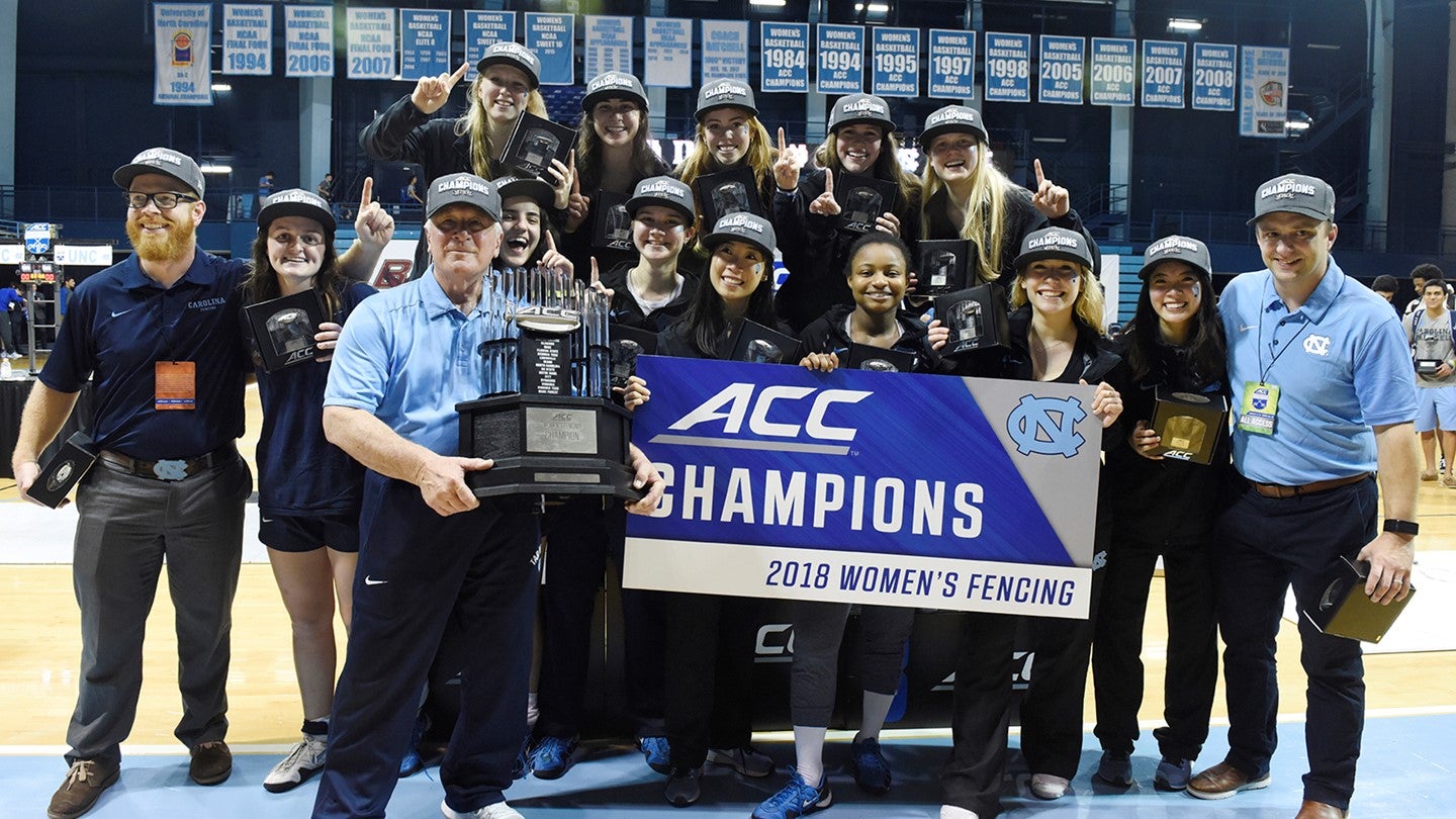 The women's fencing team holds a championship banner.