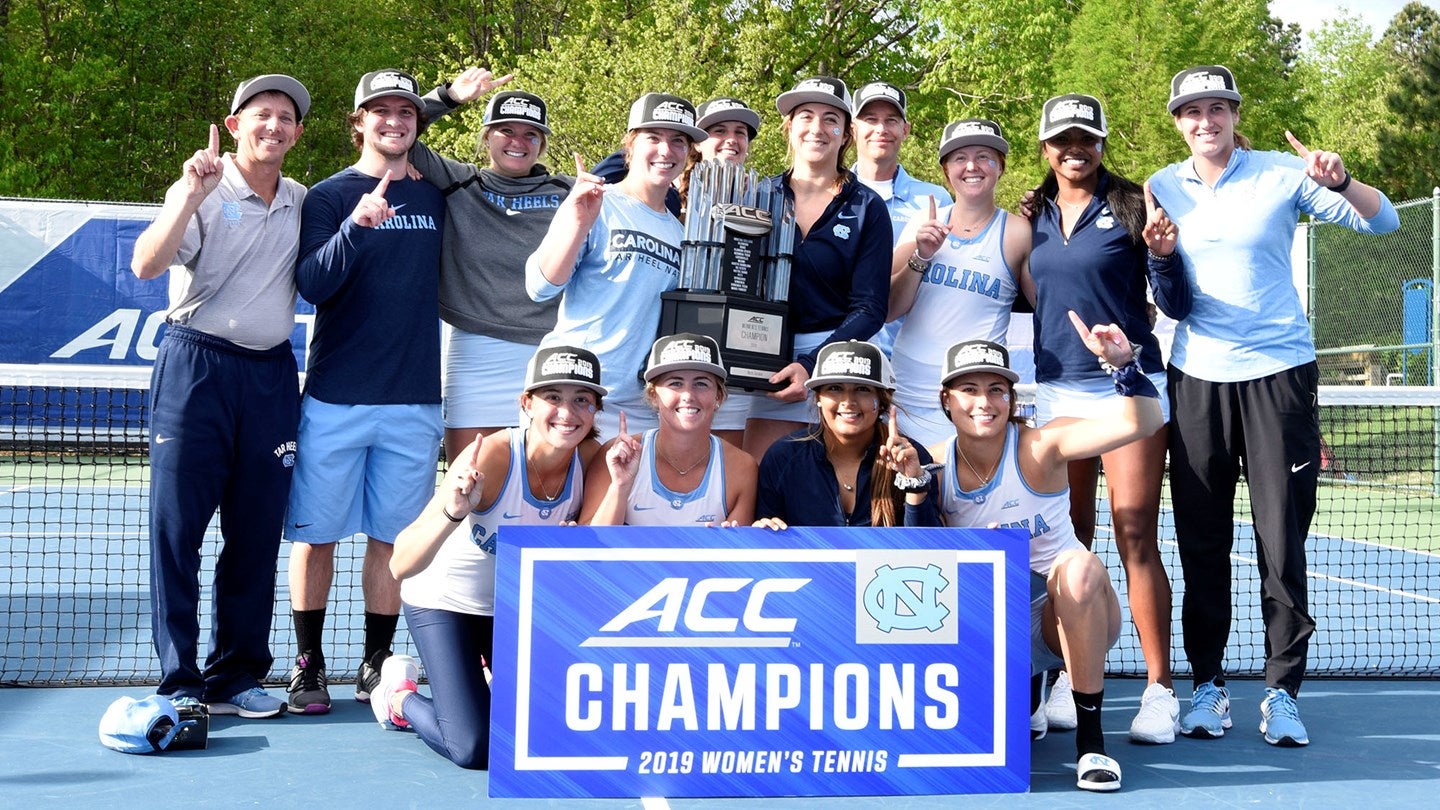 The women's tennis team holds an ACC Champions banner.