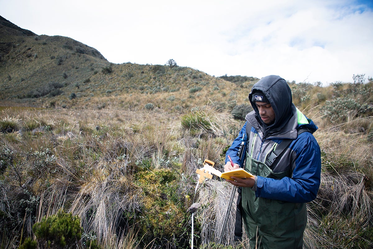 student takes notes in a field doing research.