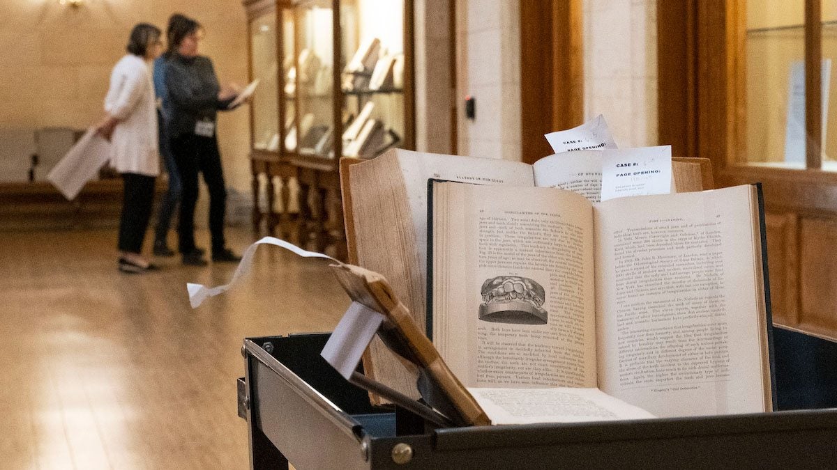 A stack of books in the foreground with people looking at a display case in the background.