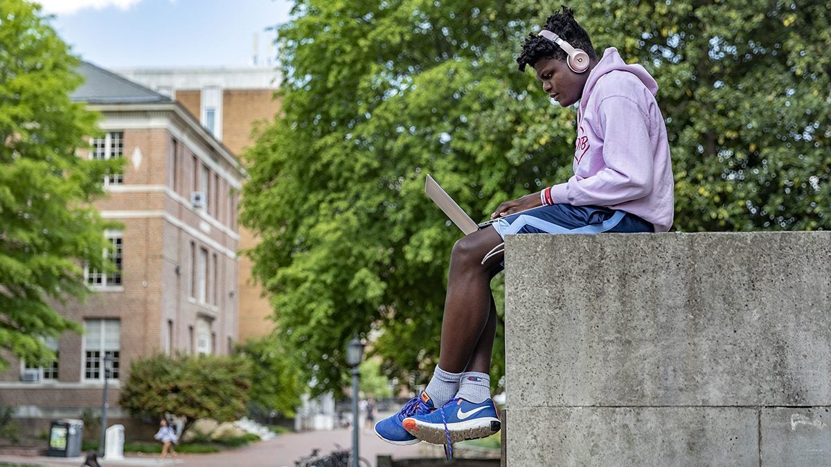 A student sits outside Wilson Library working on a laptop.