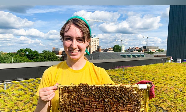 Addie Wilson holding a board with bees on it.