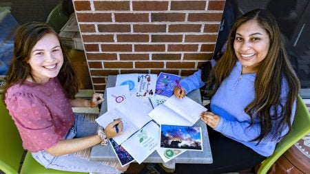 Reghan Flores and Tala Farah sit at a table with cards on it.