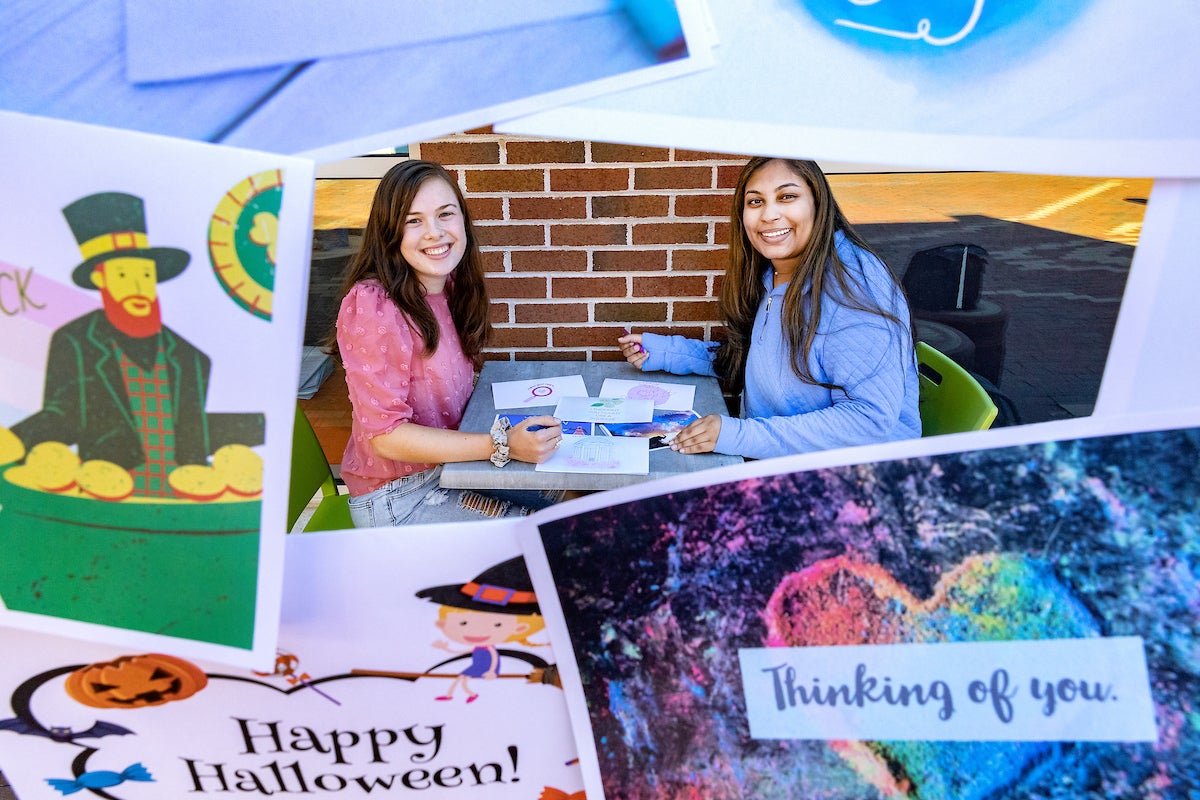 Reghan Flores and Tala Farah sit at a table with cards on it.