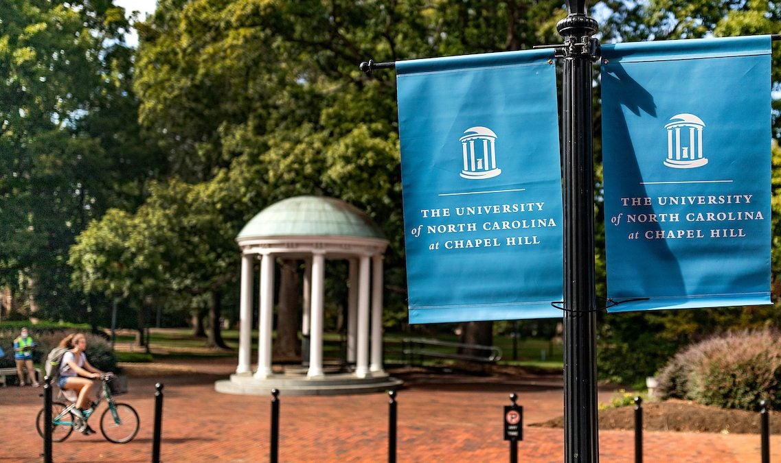 A student rides a bike past the Old Well.