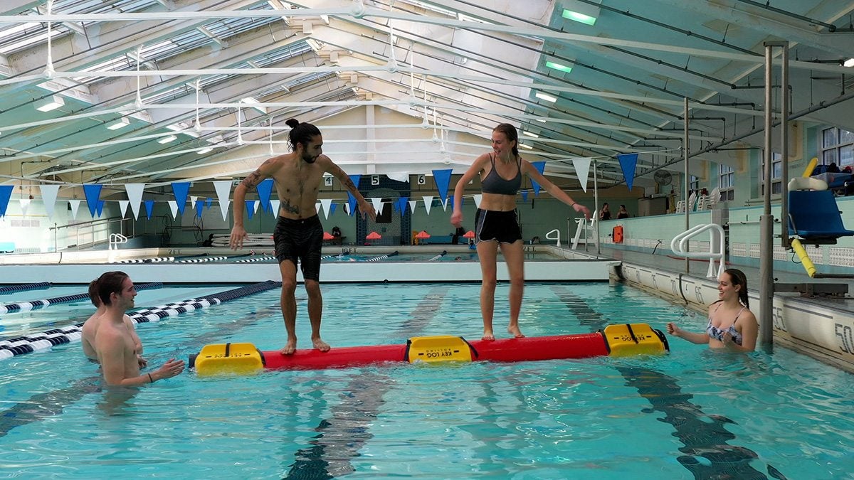 Two people on a Rolleo log in the pool.
