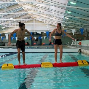 Two people on a Rolleo log in the pool.