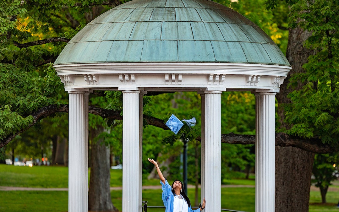 A student tosses her graduation cap into the air in front of the Old Well