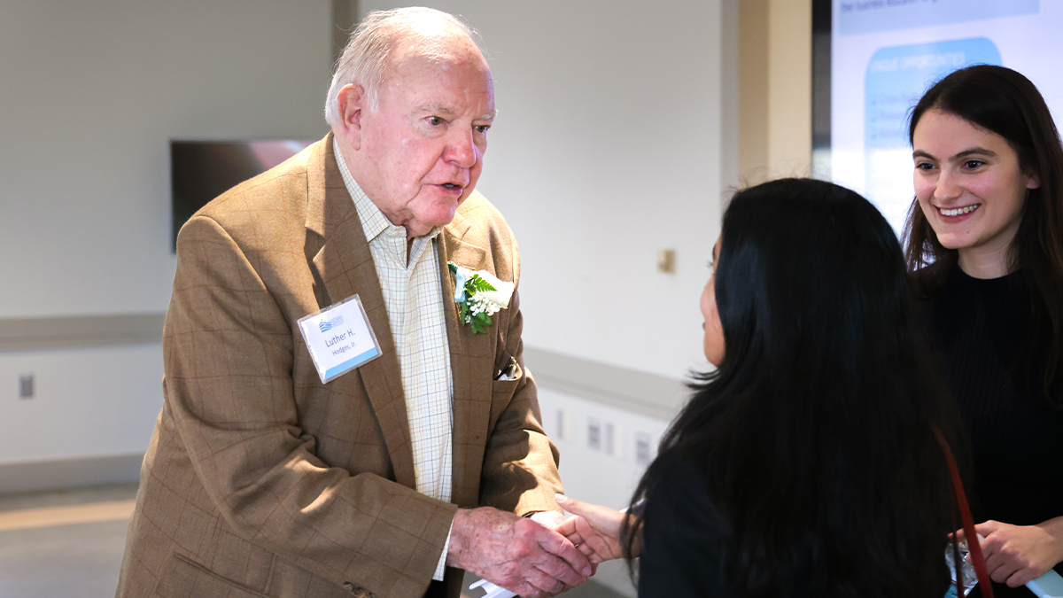 A man greeting two students and shaking hands with one of them.