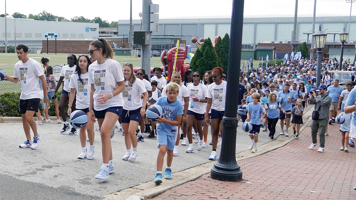 Basketball players and community members walking and dribbling basketballs across campus as part of an event to raise money for pediatric cancer research.