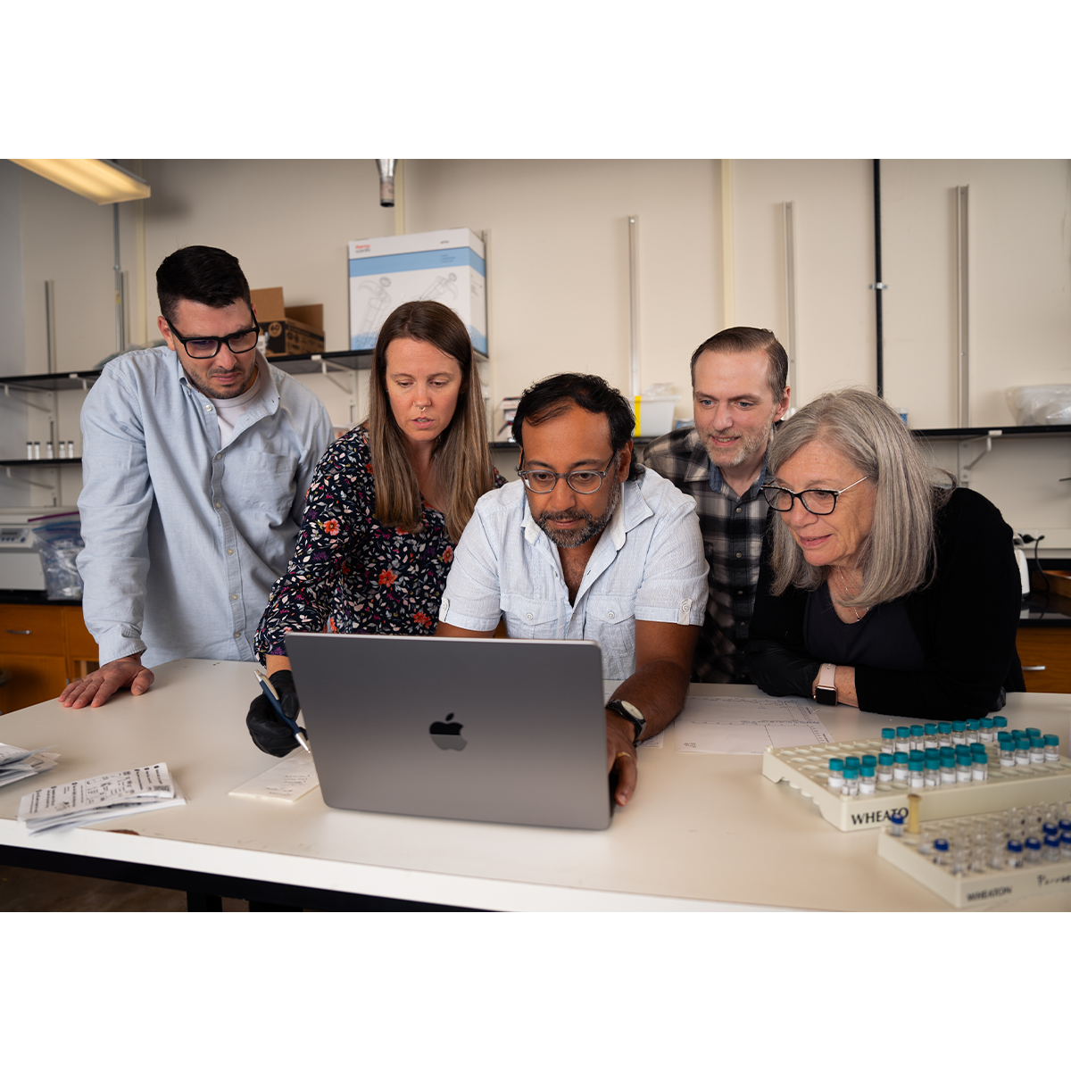 Five people huddled around a laptop in a laboratory.