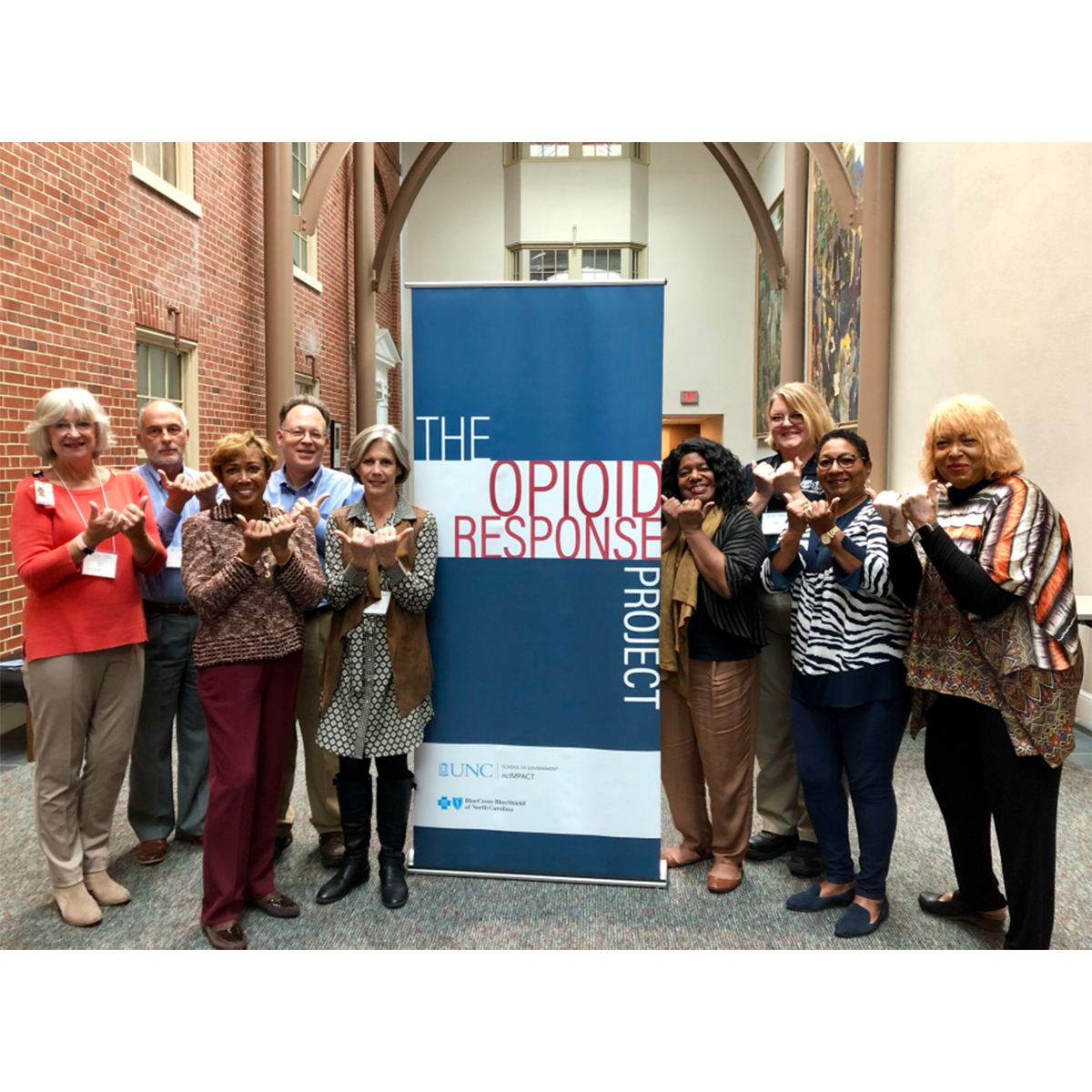 A group of nine people in Durham posing for a photo indoors in front of a sign reading 