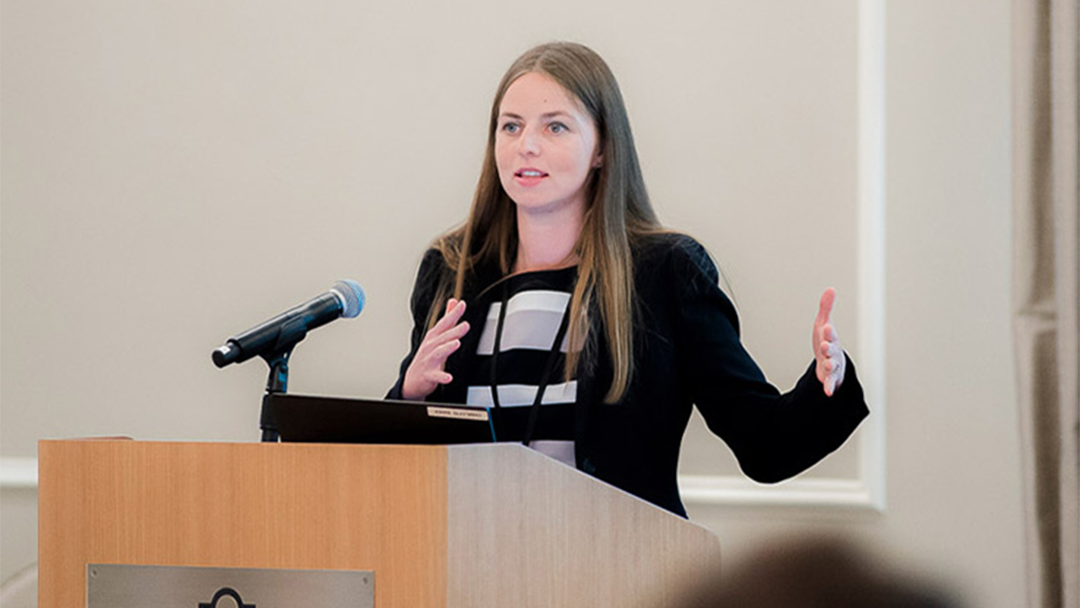 A woman stands behind a podium speaking to a crowd.