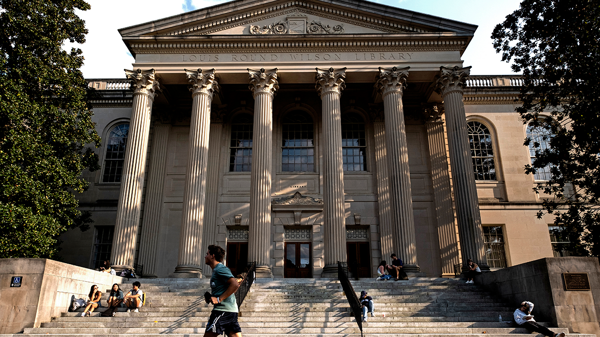 Low angle shot of Wilson Library during the day with students scattered around the front steps.