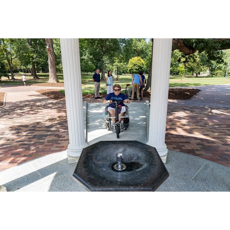 A person wheeling up the sloped pathway of the Old Well.