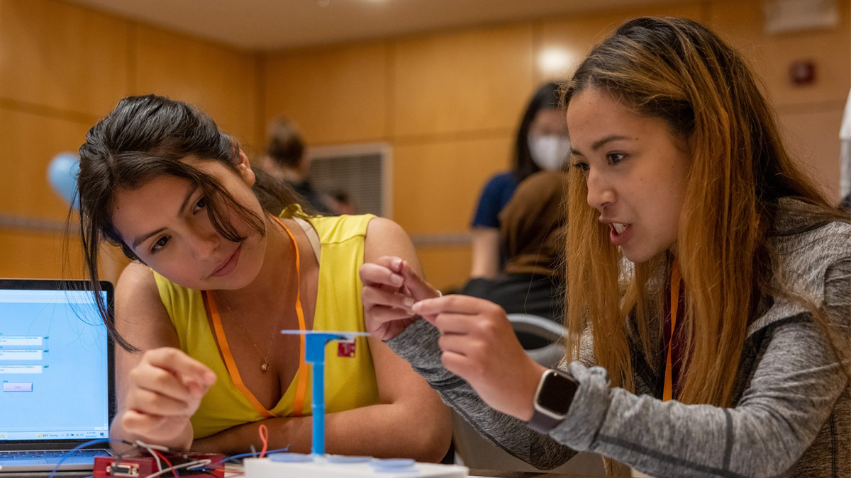 Two female students working on a project next to an open laptop.