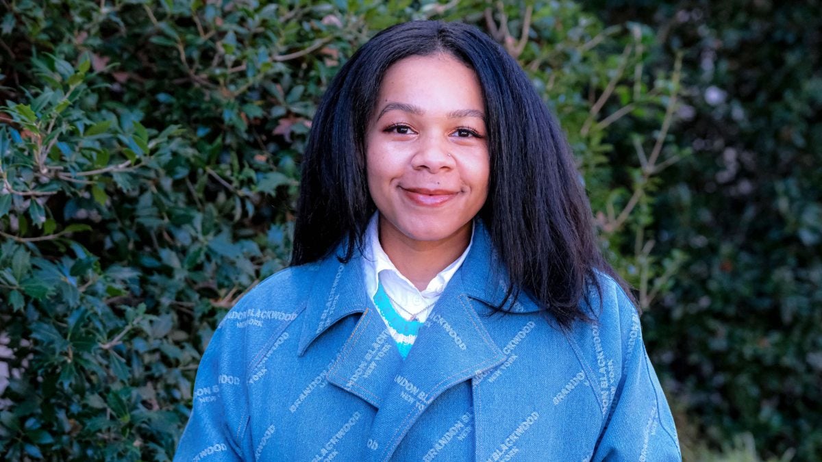 Jasmyne Yeldell standing in front of bushes with blue jacket on.