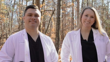 Cy and Kandis Fogleman wearing lab coats and black shirts in front of bare trees.