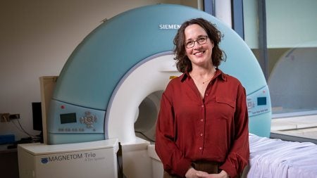 Stephanie Engel wearing red shirt and standing in front of MRI machine.