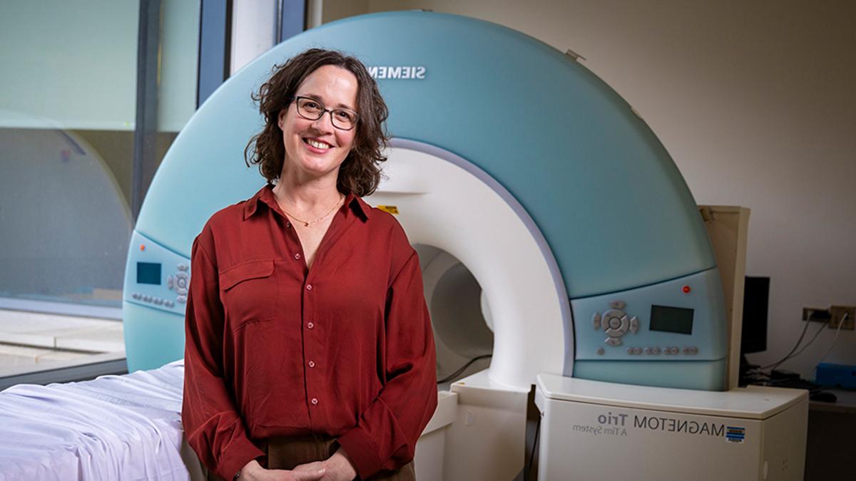 Stephanie Engel wearing red shirt and standing in front of MRI machine.