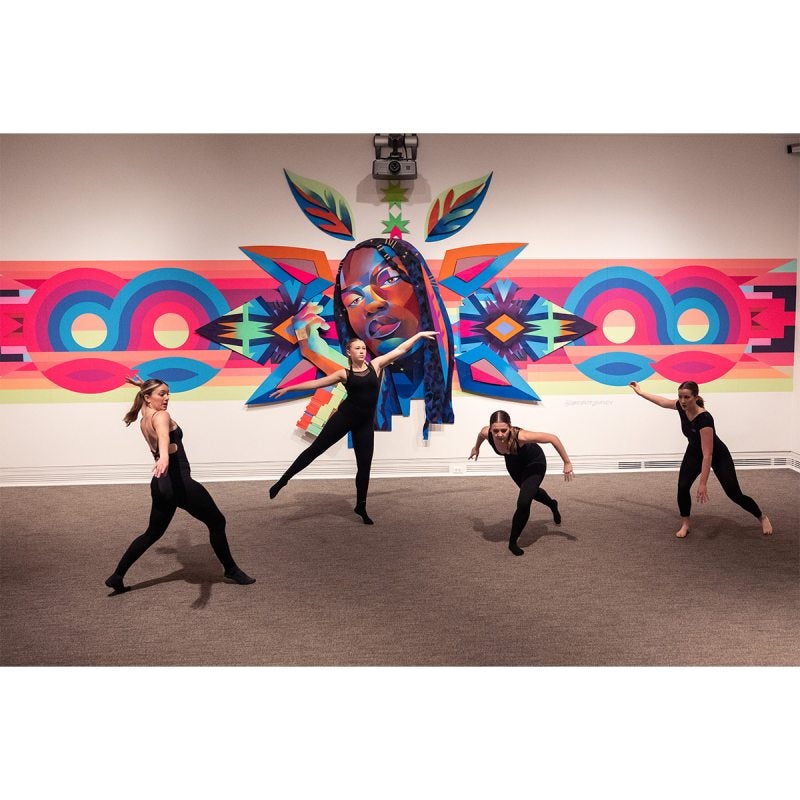 Dancers dancing in front of a large tapestry art display.