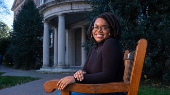 Dezja Ishmeal sitting on a bench on U.N.C. campus with the Old Well in the background.