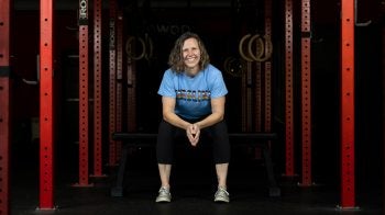 Kara Hume sitting at a workout bench surrounded by workout racks.