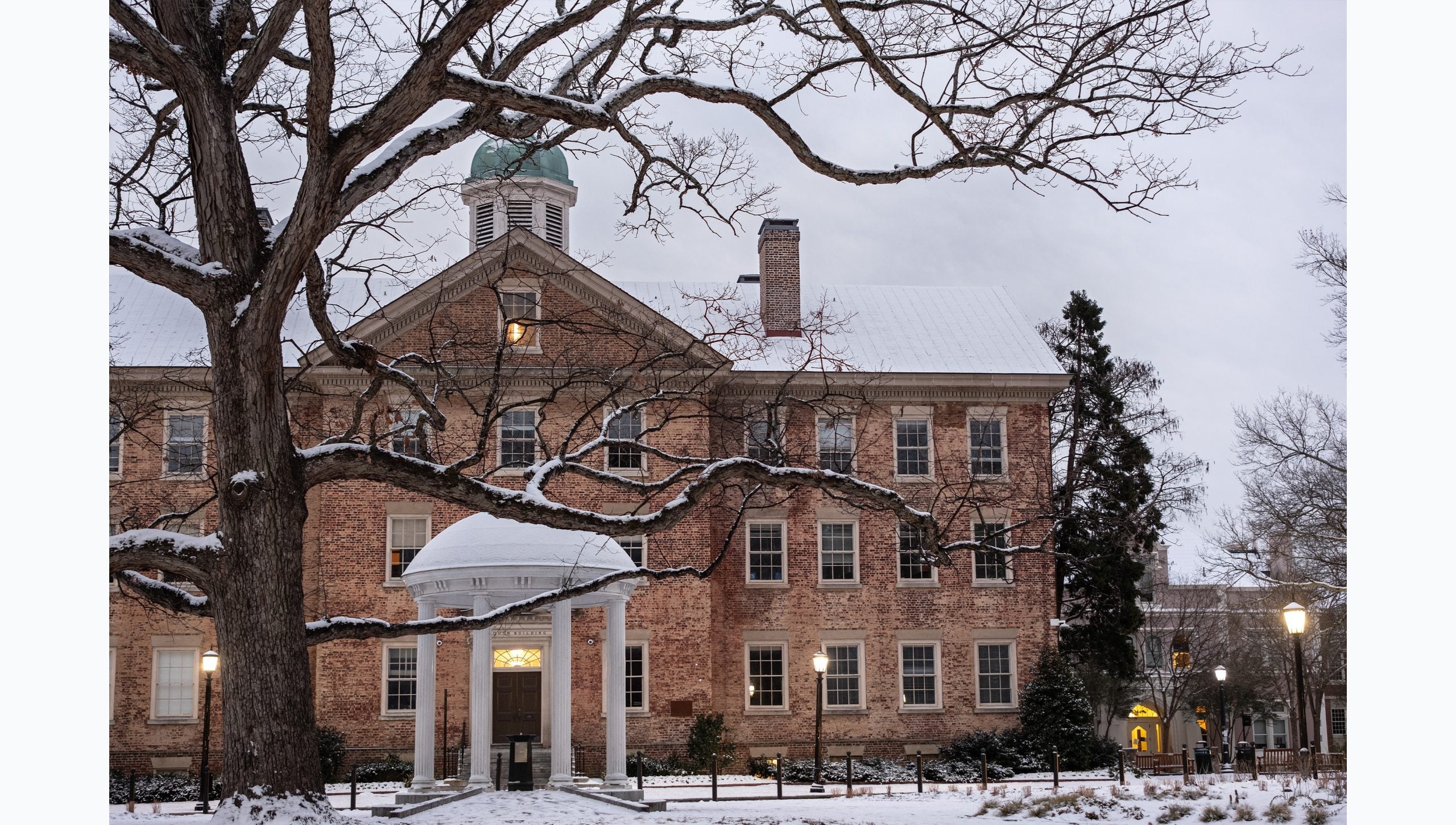 Morning photo of a snow-covered Old Well with South Building seen in the background on the campus of U.N.C Chapel Hill.