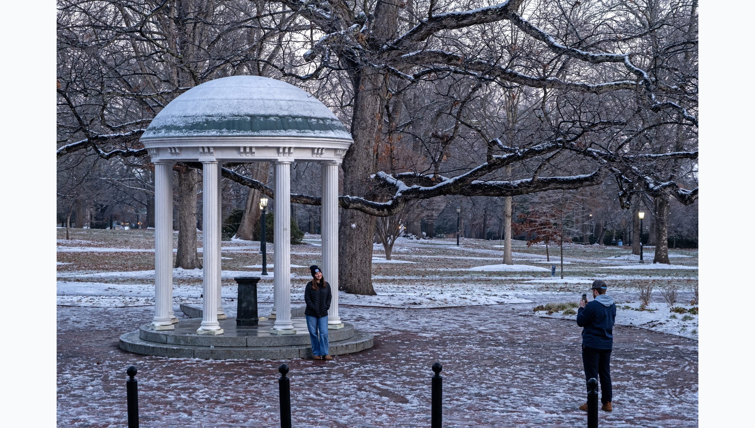 A student having her photo taken in front of the Old Well on the snow-covered campus of U.N.C Chapel Hill campus.
