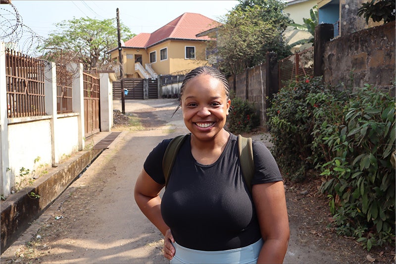 Gina Adatsi smiling and posing on small street in a Sierra Leone neighborhood.