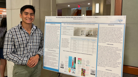 Man standing next to poster board with graphics and text on it.