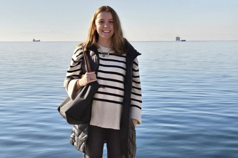 Katherine Eltz standing in front of a waterfront in Greece.