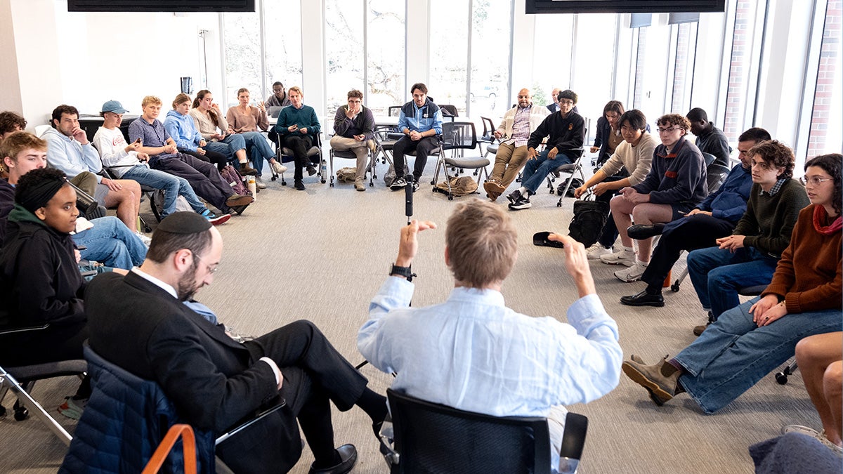 Students sit in a circle and listen to a professor talk