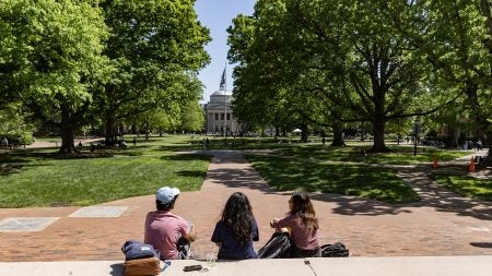 Three students sitting on the steps of South Building facing Wilson Library and Polk Place on the campus of UNC-Chapel Hill.