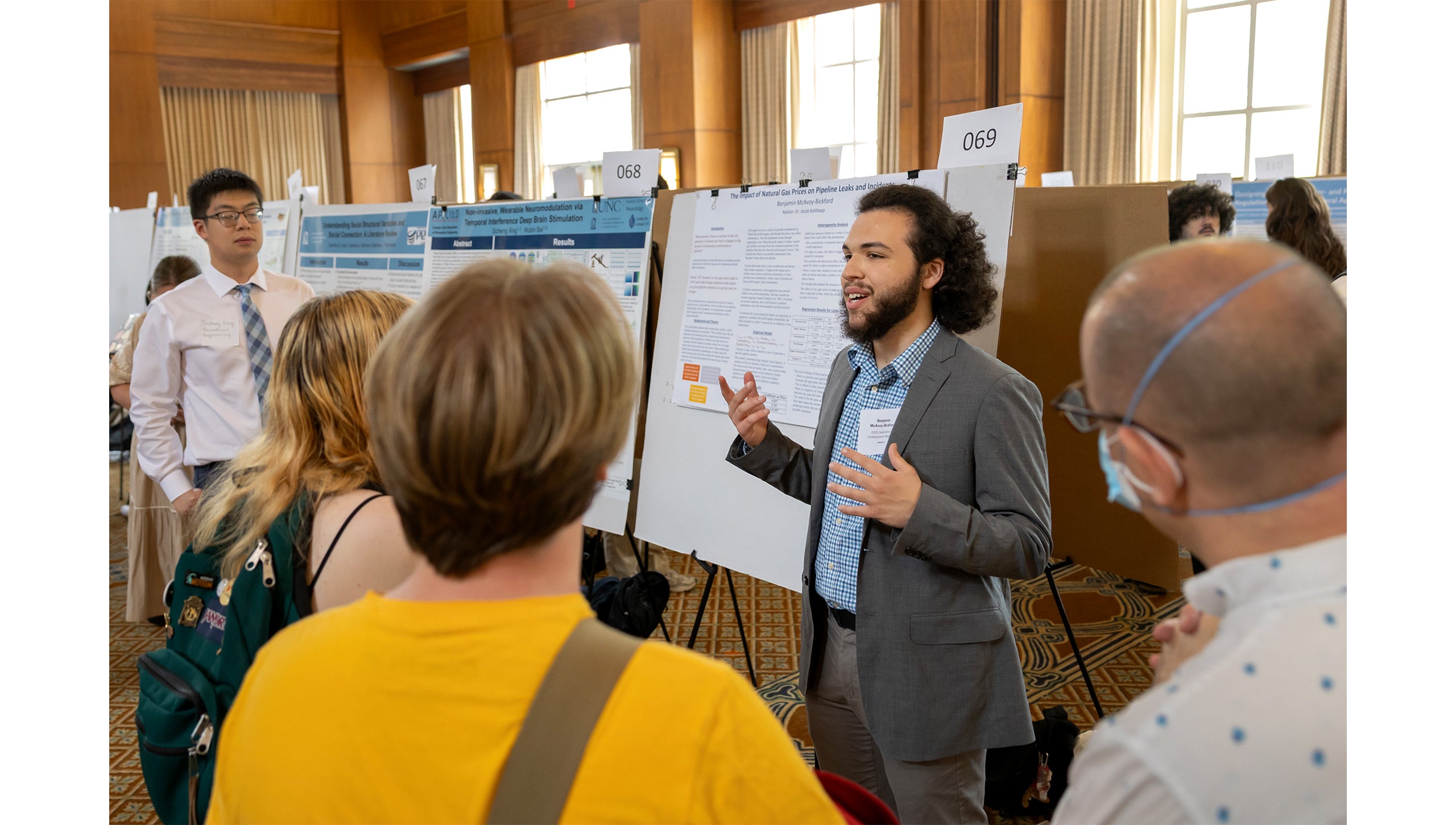 A student explains his research in front of a poster at the Celebration of Undergraduate Research