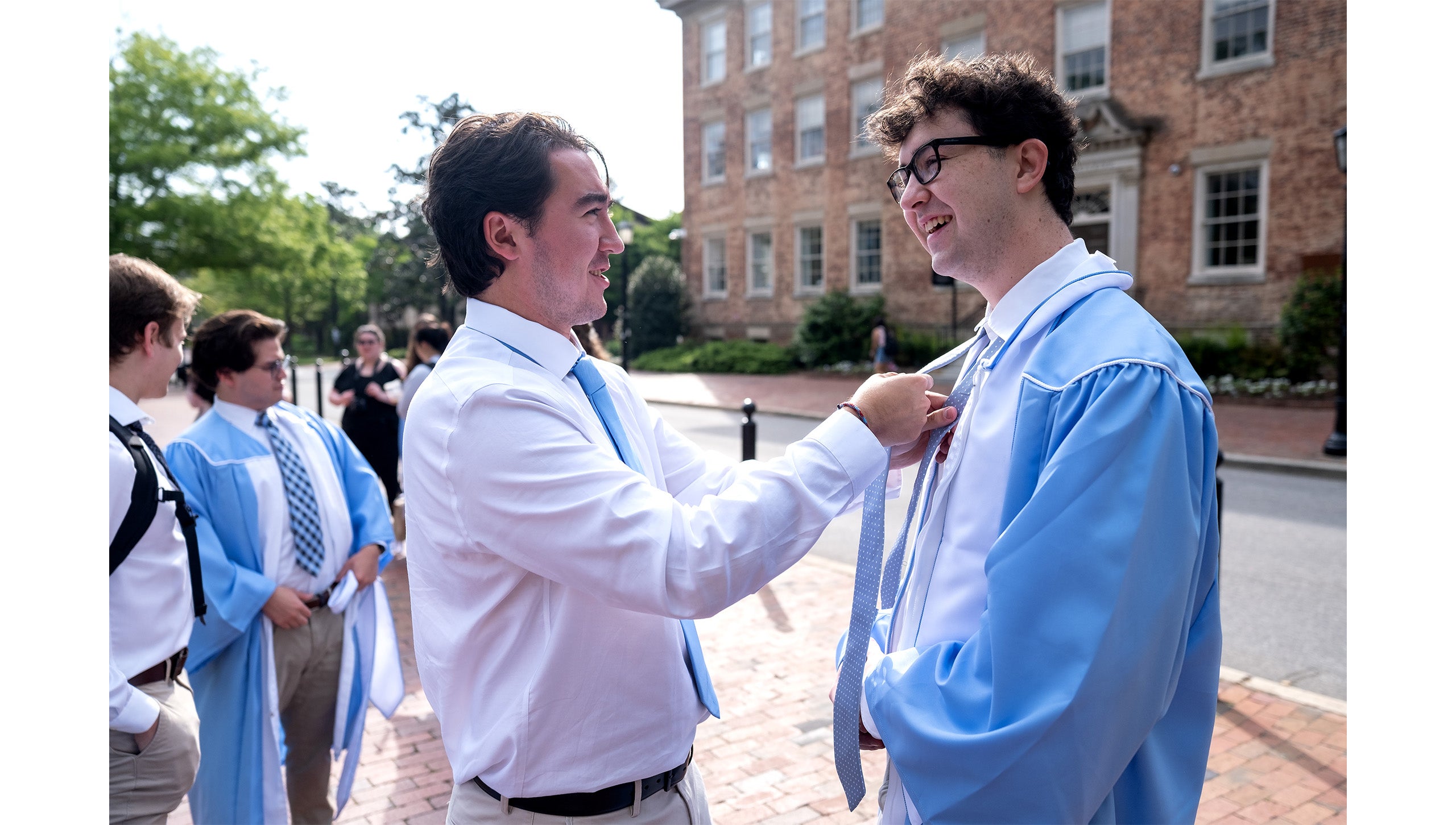 Carolina student helps tie a graduate's tie before taking Commencement photos by the Old Well
