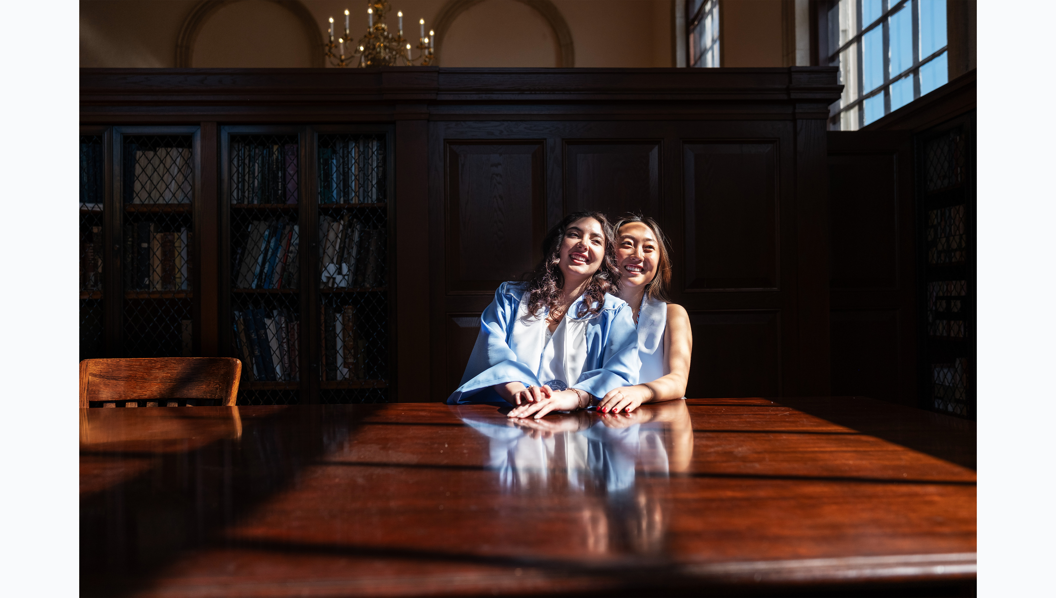 Two UNC-Chapel Hill students sitting at a table in Wilson Library's Fearrington Reading Room posing for graduation photos.