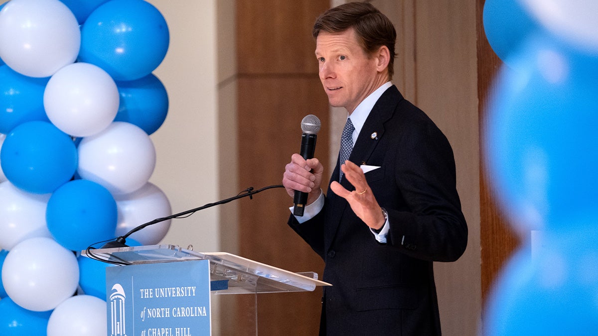 Chancellor Lee H. Robert speaking into a microphone at a podium at UNC-Chapel Hill's Public Service Awards. Carolina Blue and white balloons are seen in the background.