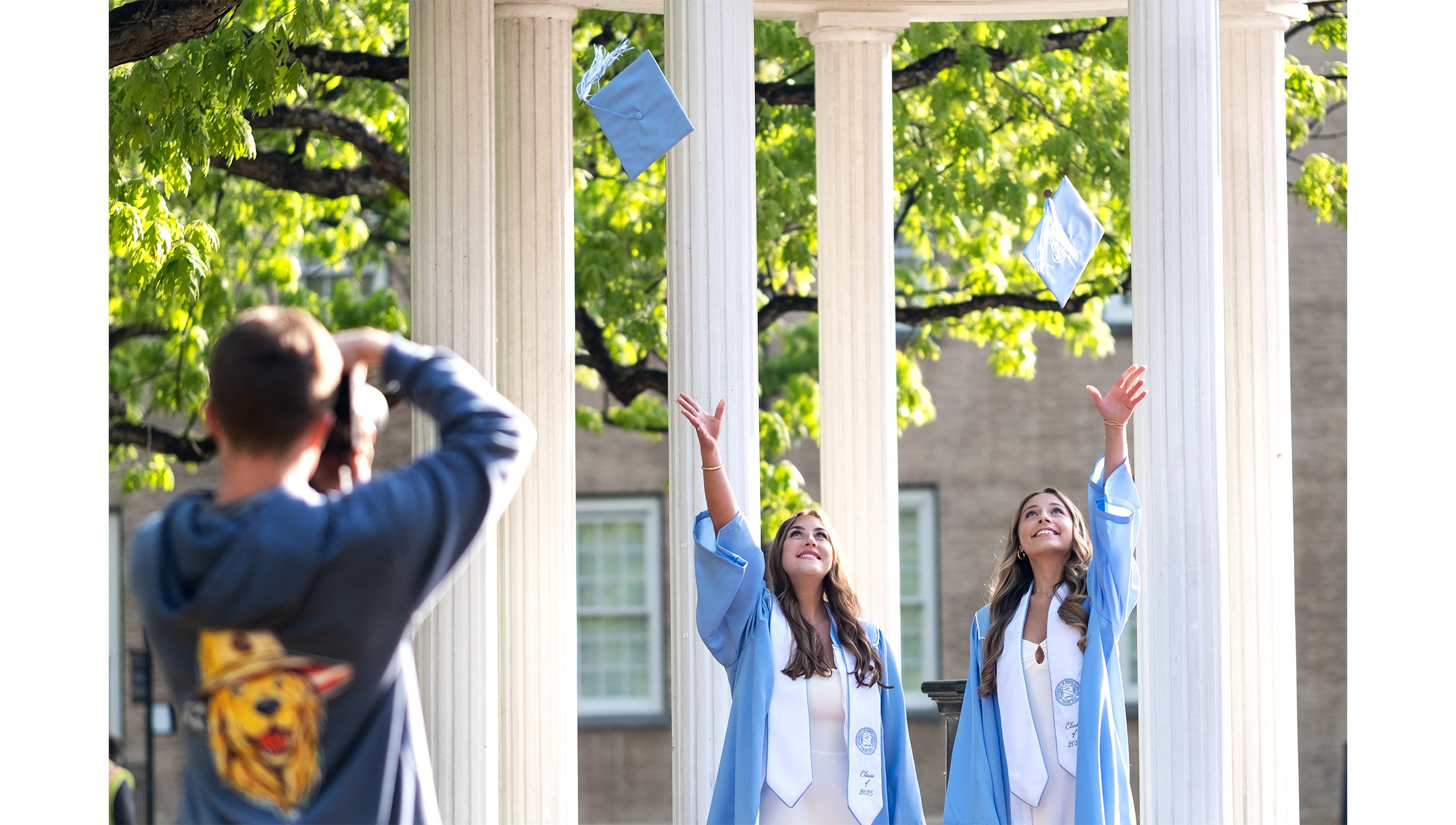 Graduates throw their caps in the air while posing for a photo in front of the Old Well