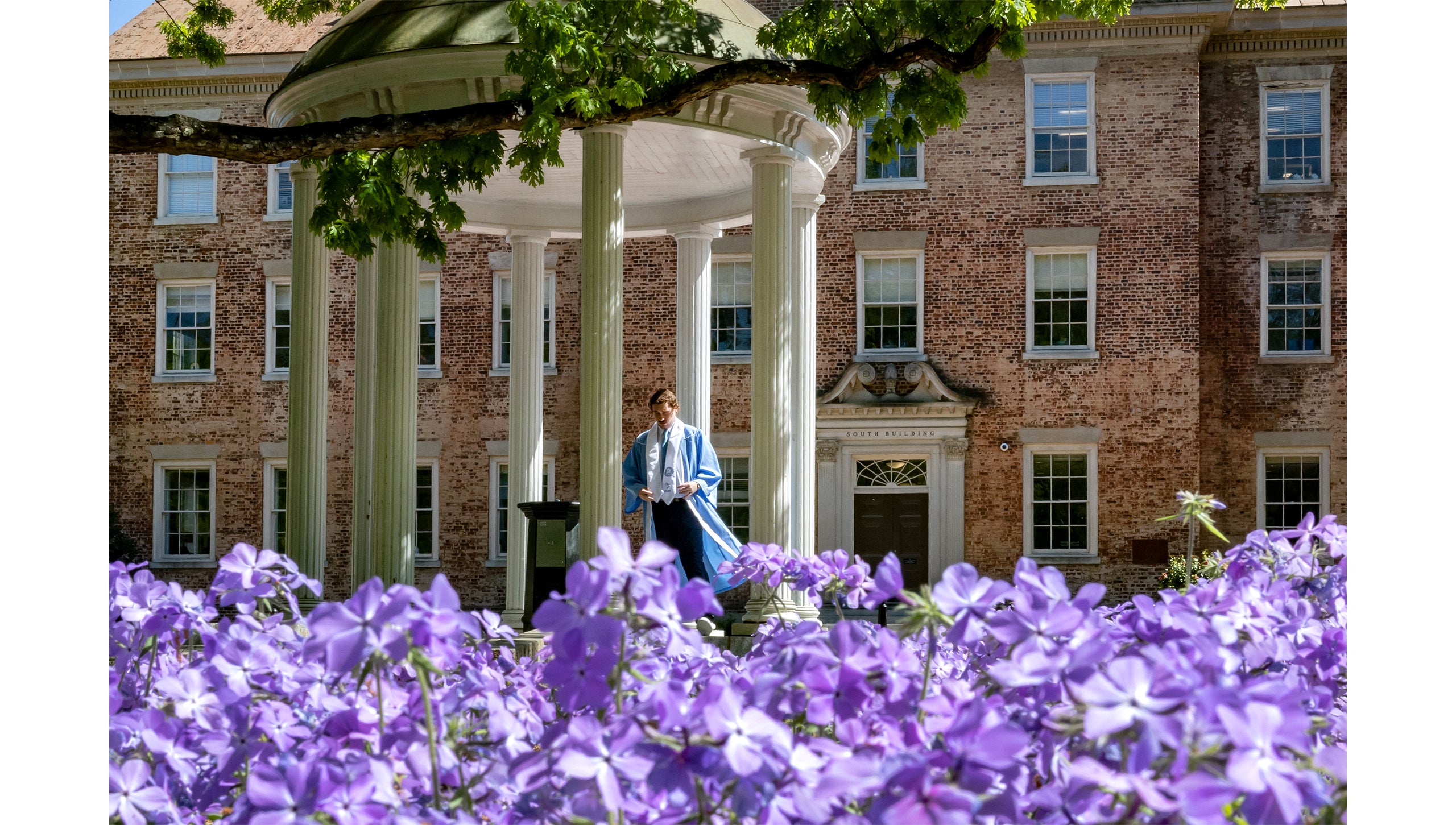 Spring flowers in front of the Old Well, as a graduate in cap and gown walks in the background