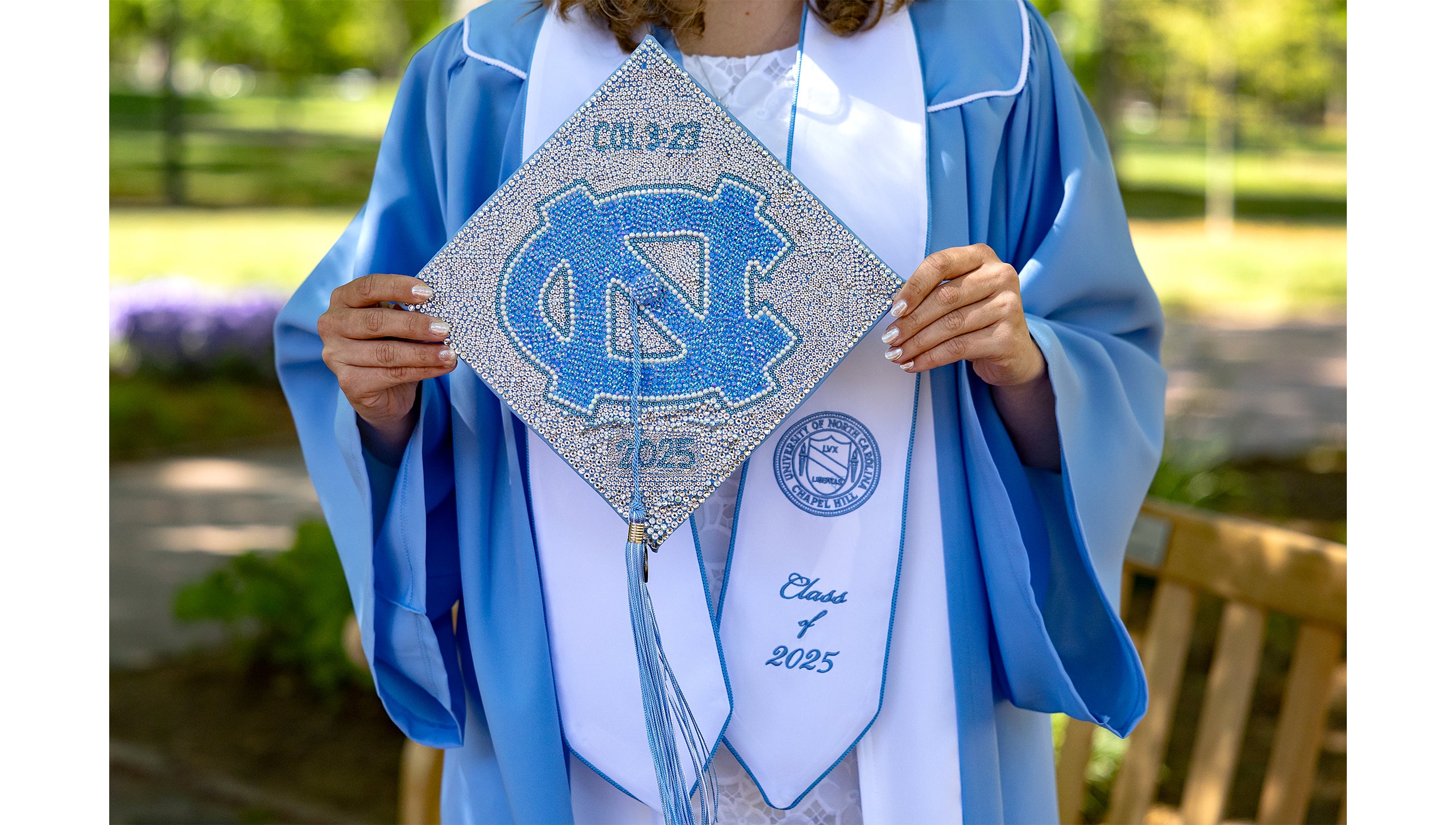 A graduate holds her decorated graduation cap, bedazzled with a UNC logo.