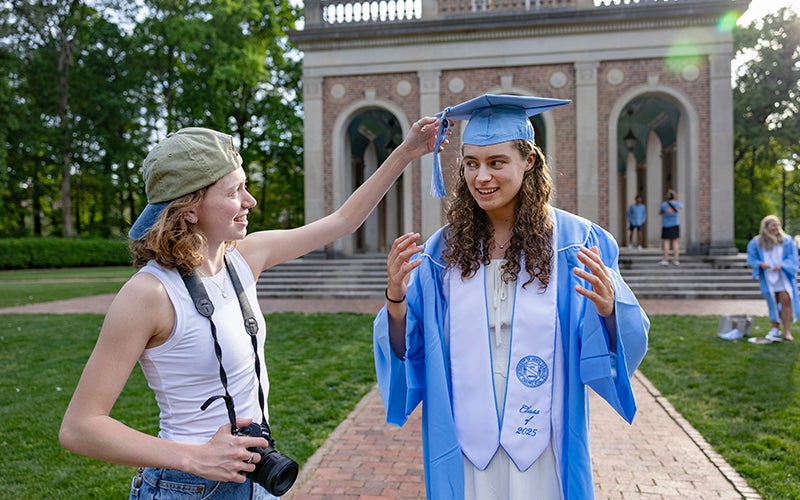 A photographer helps a graduate straighten their cap before taking photos at the Bell Tower.